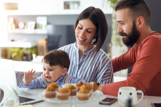 Beautiful young parents with they baby looking cartoons on lapto